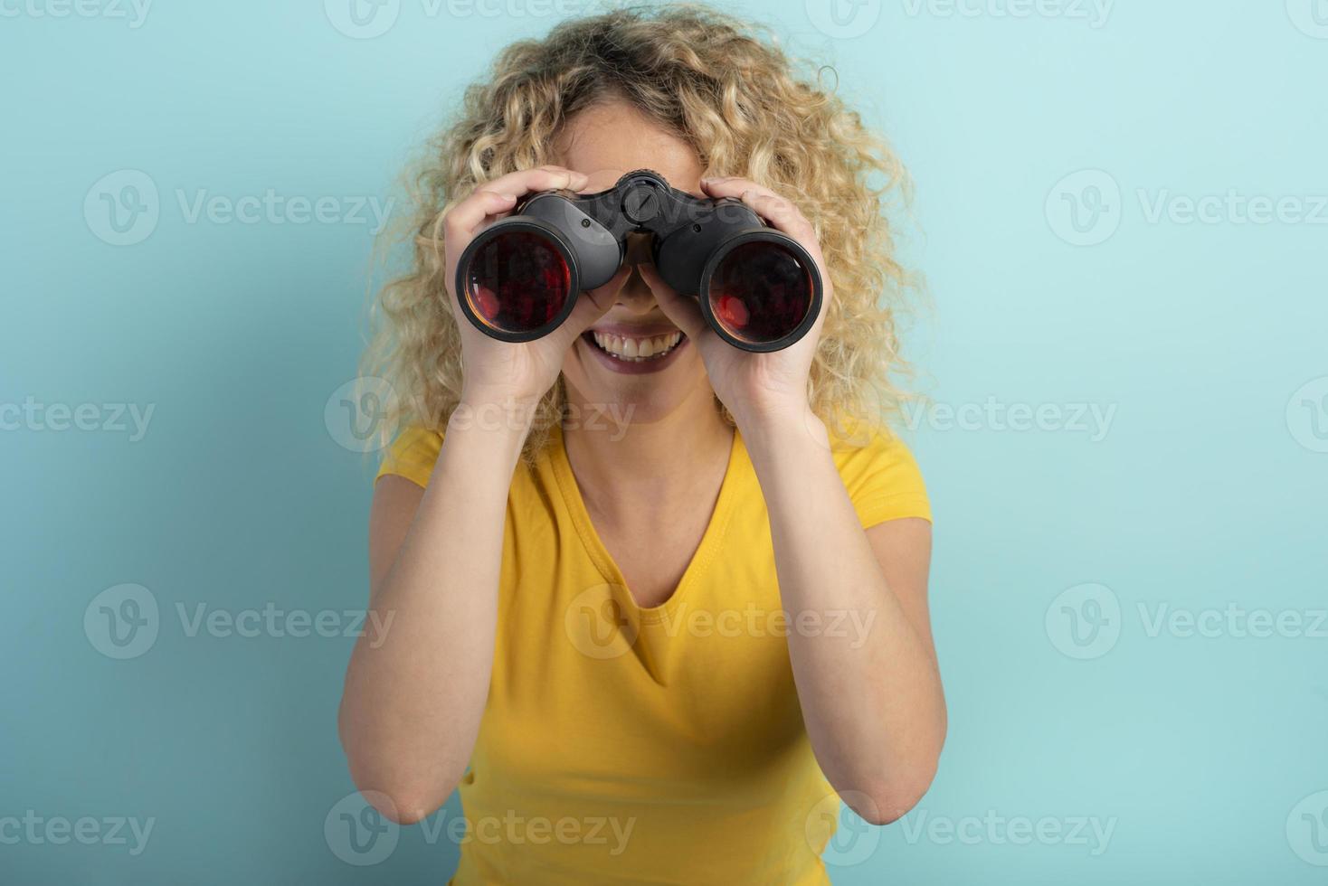 Happy girl looks with binocular something. Cyan background photo