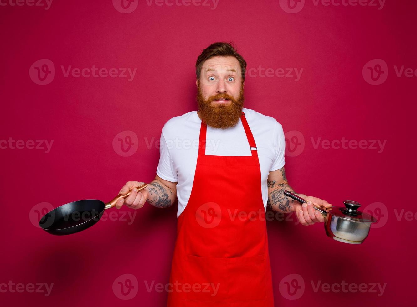 afraid chef with beard and red apron cooks with pan and pot photo