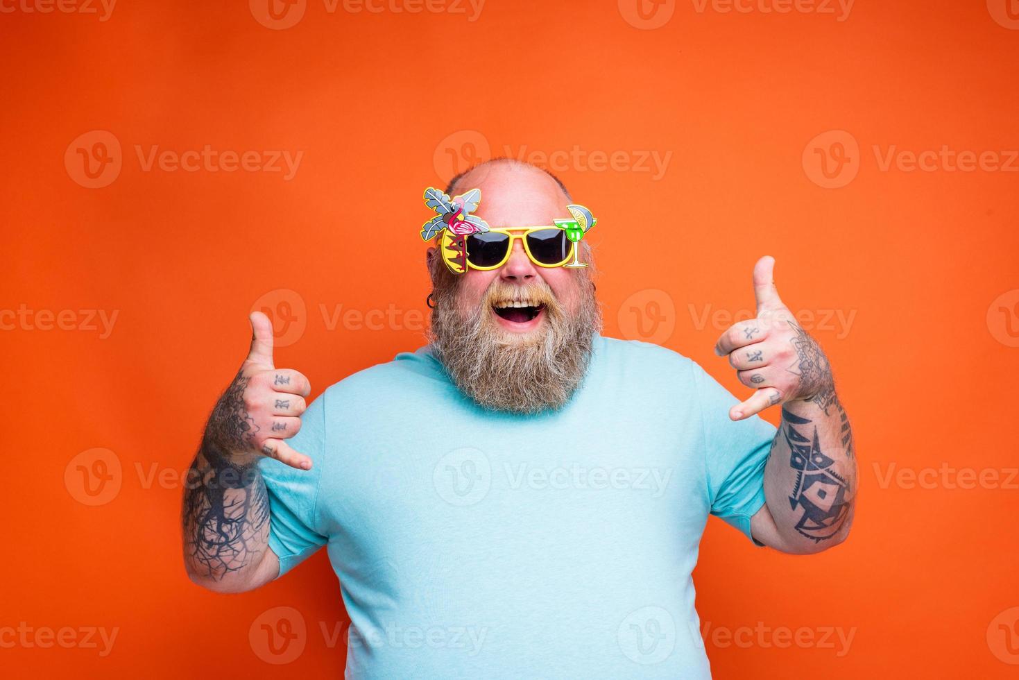 Fat happy man with beard, tattoos and sunglasses is ready for the summer photo