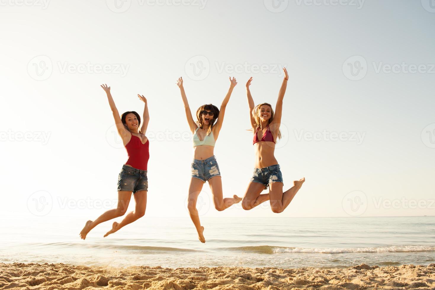 Happy smiling friends jumping at the beach photo