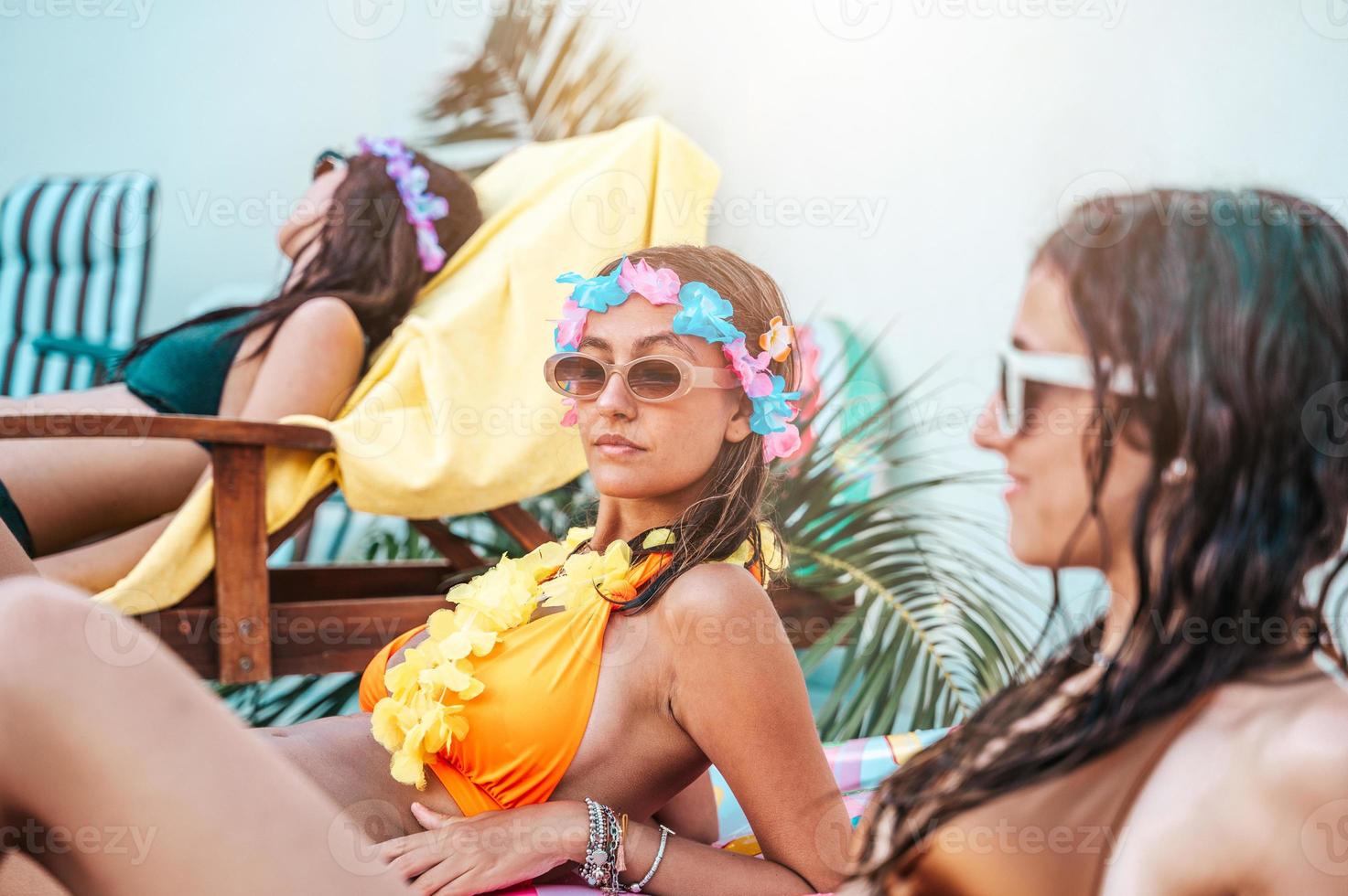 Group of friends tan and relax on the deck chairs at swimming pool photo