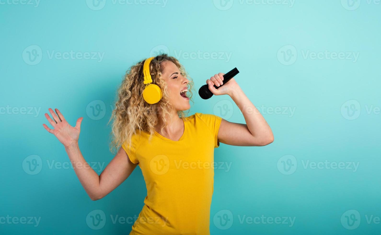 Girl with headset listens to music and song with microphone. emotional and energetic expression. Cyan background photo