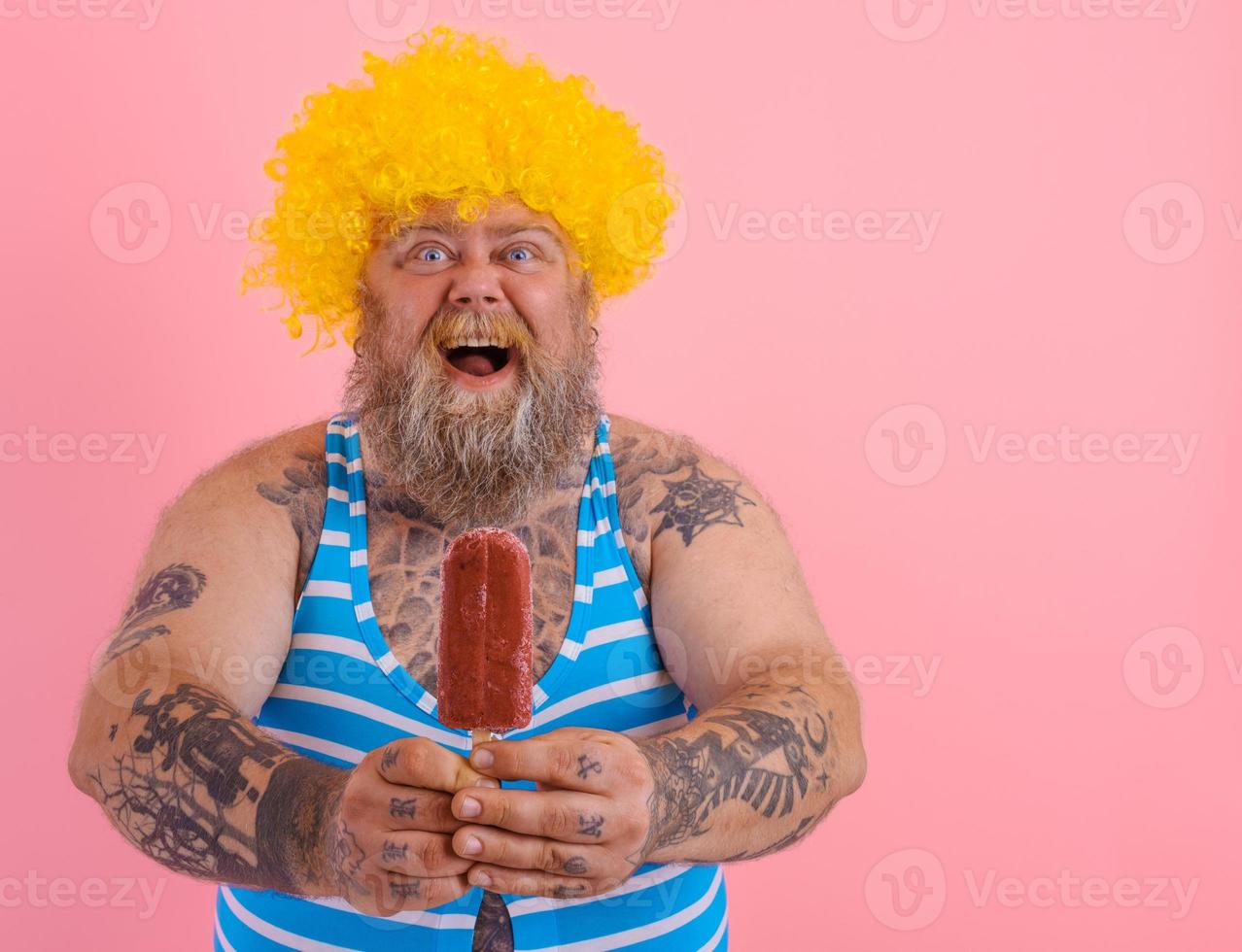 Fat amazed man with beard and wig eats a popsicle photo