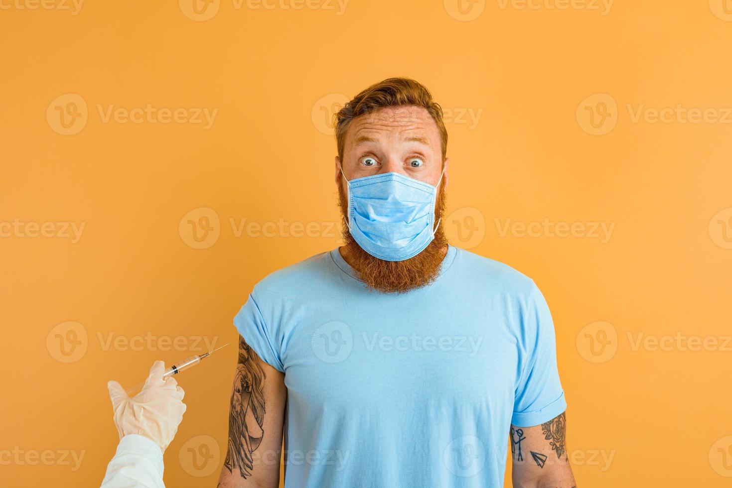 Afraid man with beard, tattoo and mask for covid-19 is ready for the virus vaccine photo