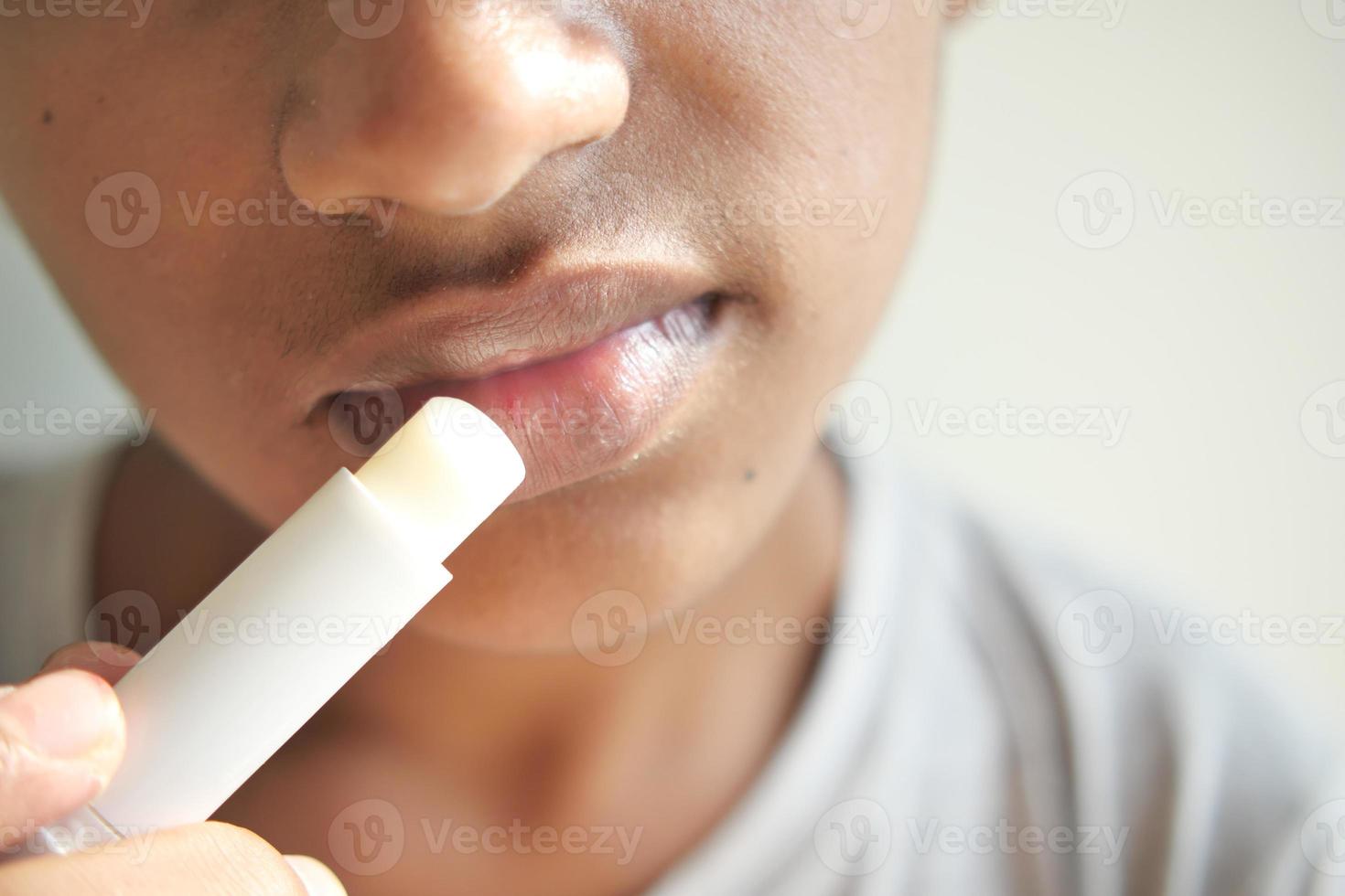 joven aplicando bálsamo labial hidratante en los labios foto