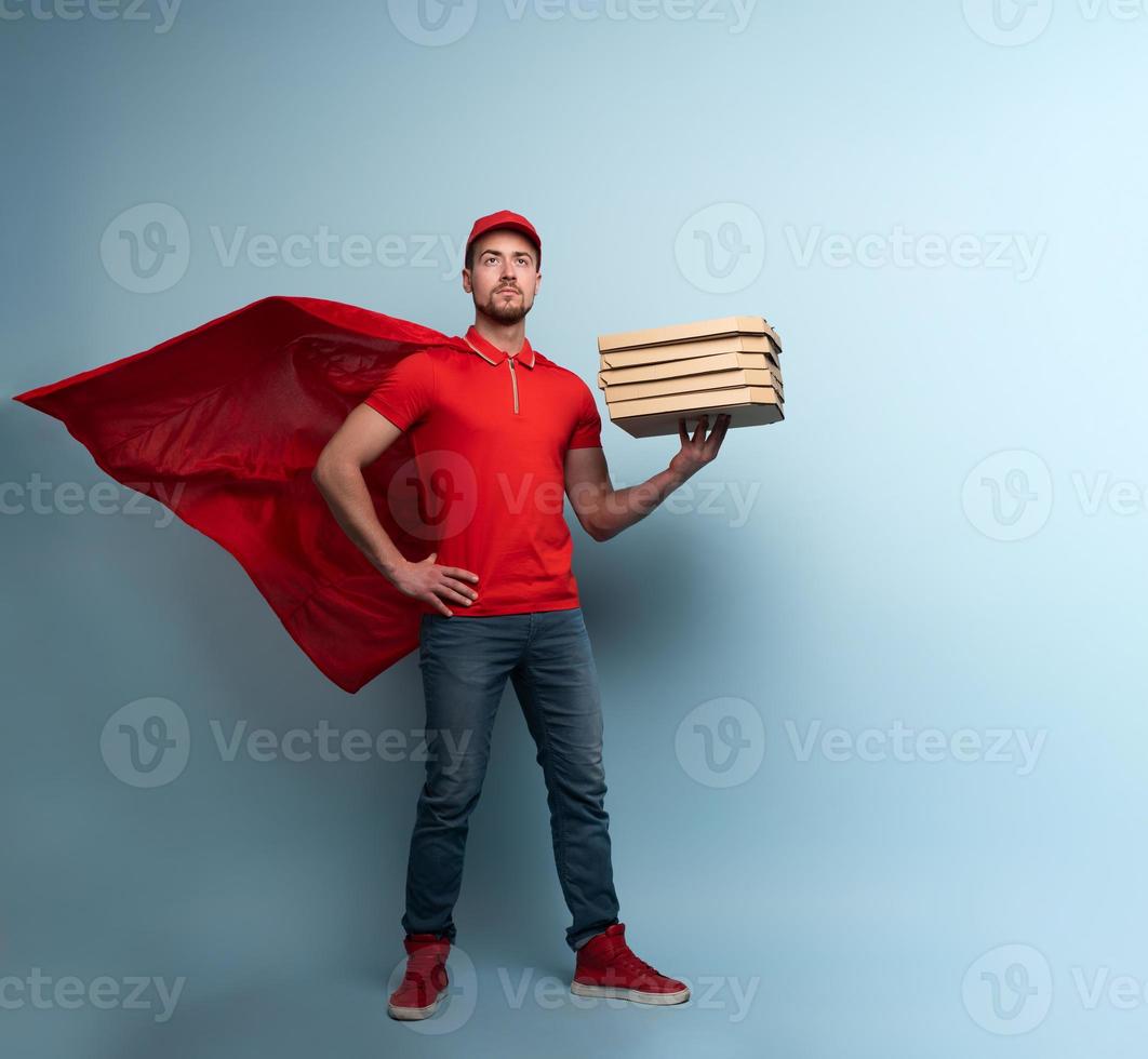 Deliveryman with pizzas acts like a powerful superhero. Concept of success and guarantee on shipment. Studio cyan background photo