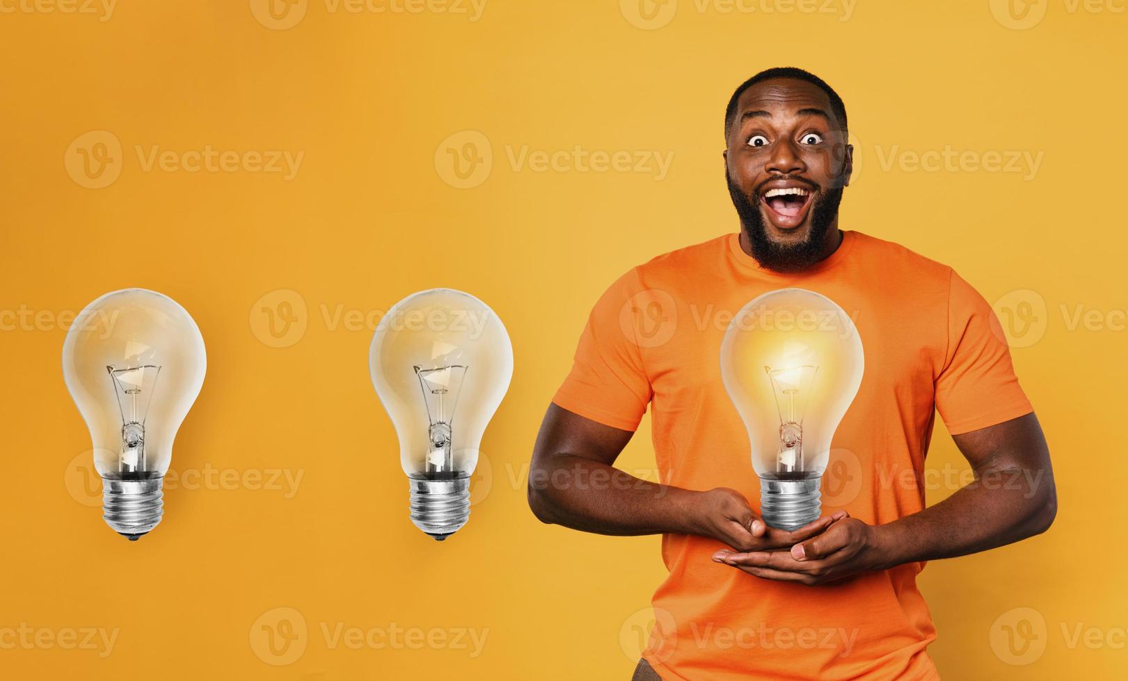 Happy afro man holds a lightbulb with hands. Concept of idea and creativity. Orange background photo