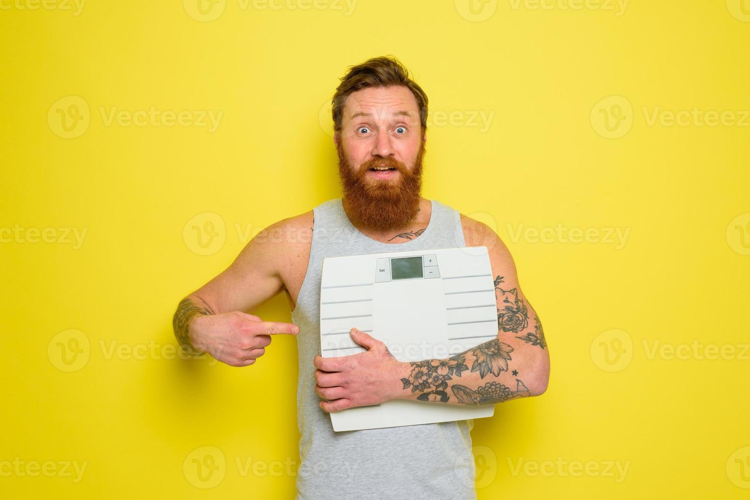 Amazed man with beard and tattoos holds an electronic balance photo
