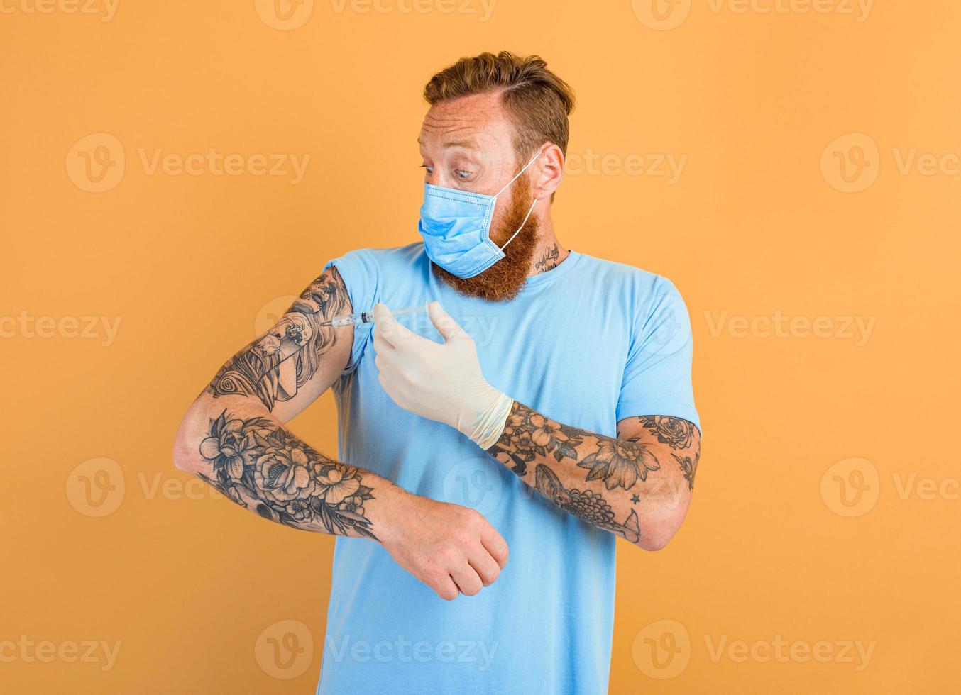 Afraid man with beard, tattoo and mask for covid-19 is ready for the virus vaccine photo