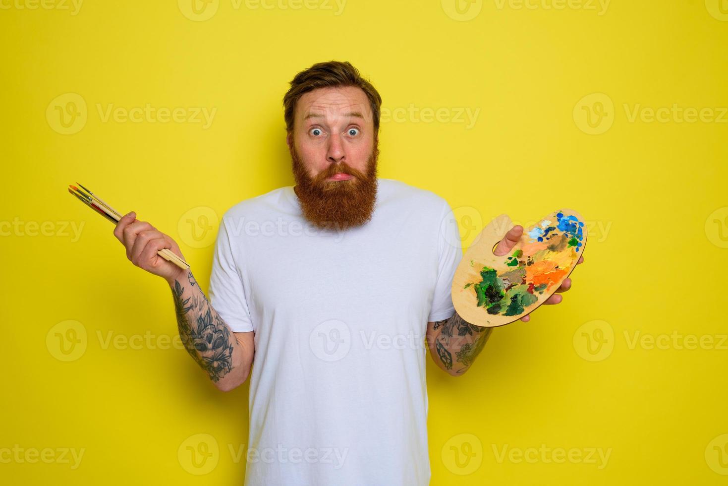 Undecided man with beard and tattoo is ready to draw with brushes photo