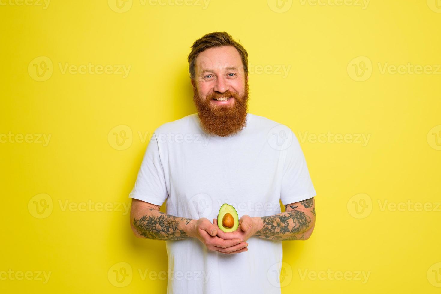 Happy man with beard and tattoos holds an avocado photo