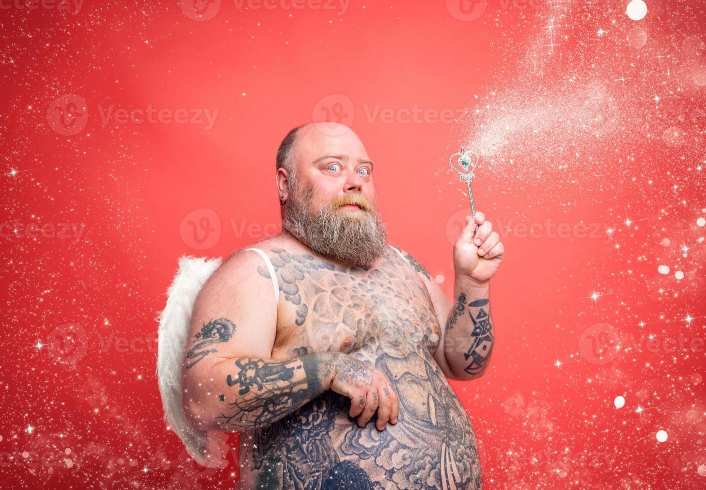 Fat thoughtful man with beard ,tattoos and wings acts like an magic fairy photo