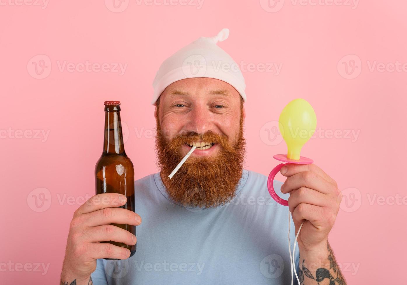 Happy man with beard and tattoos acts like a little newborn baby with beer in hand photo