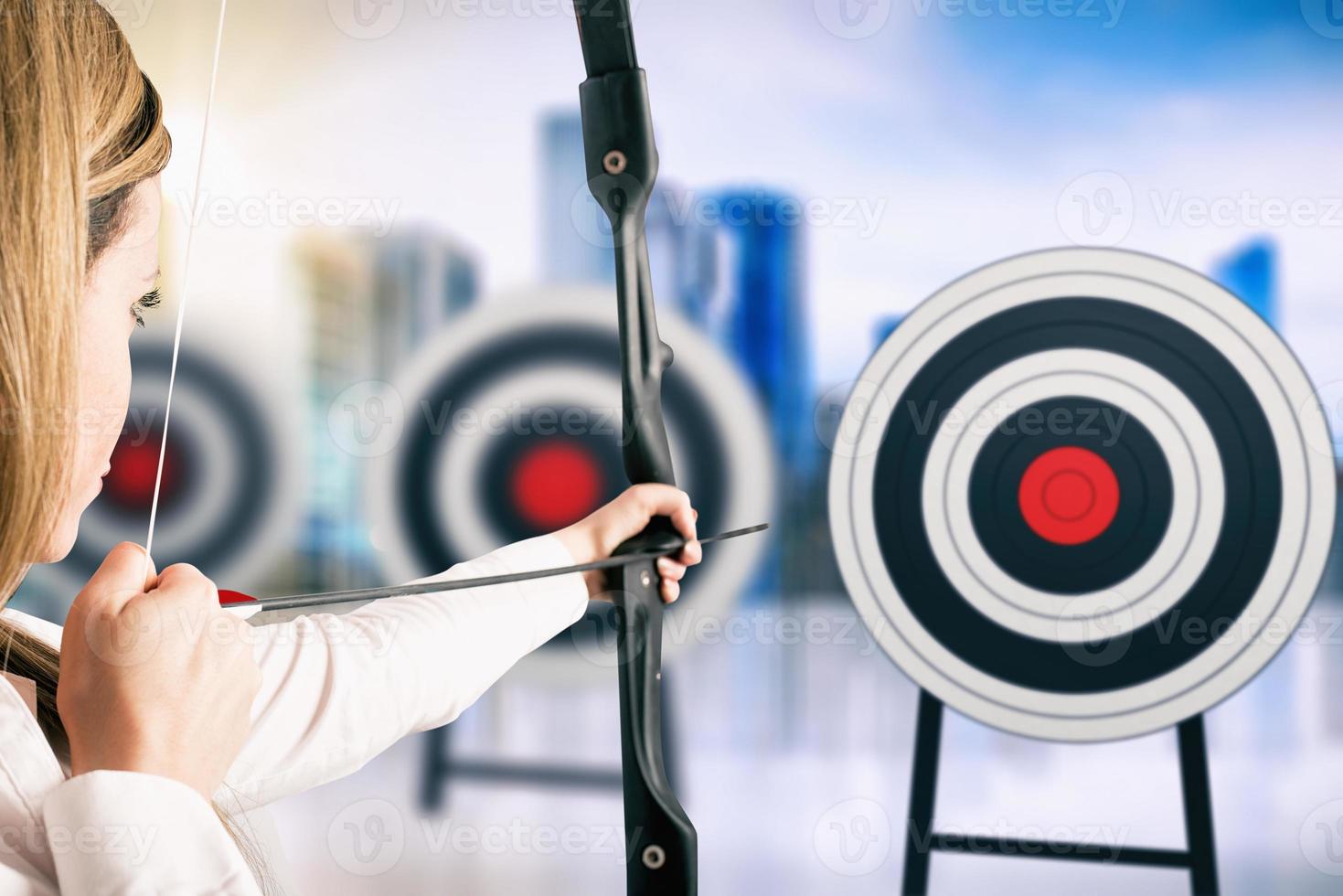 Businesswoman with bow and arrow pointing the center of the target photo