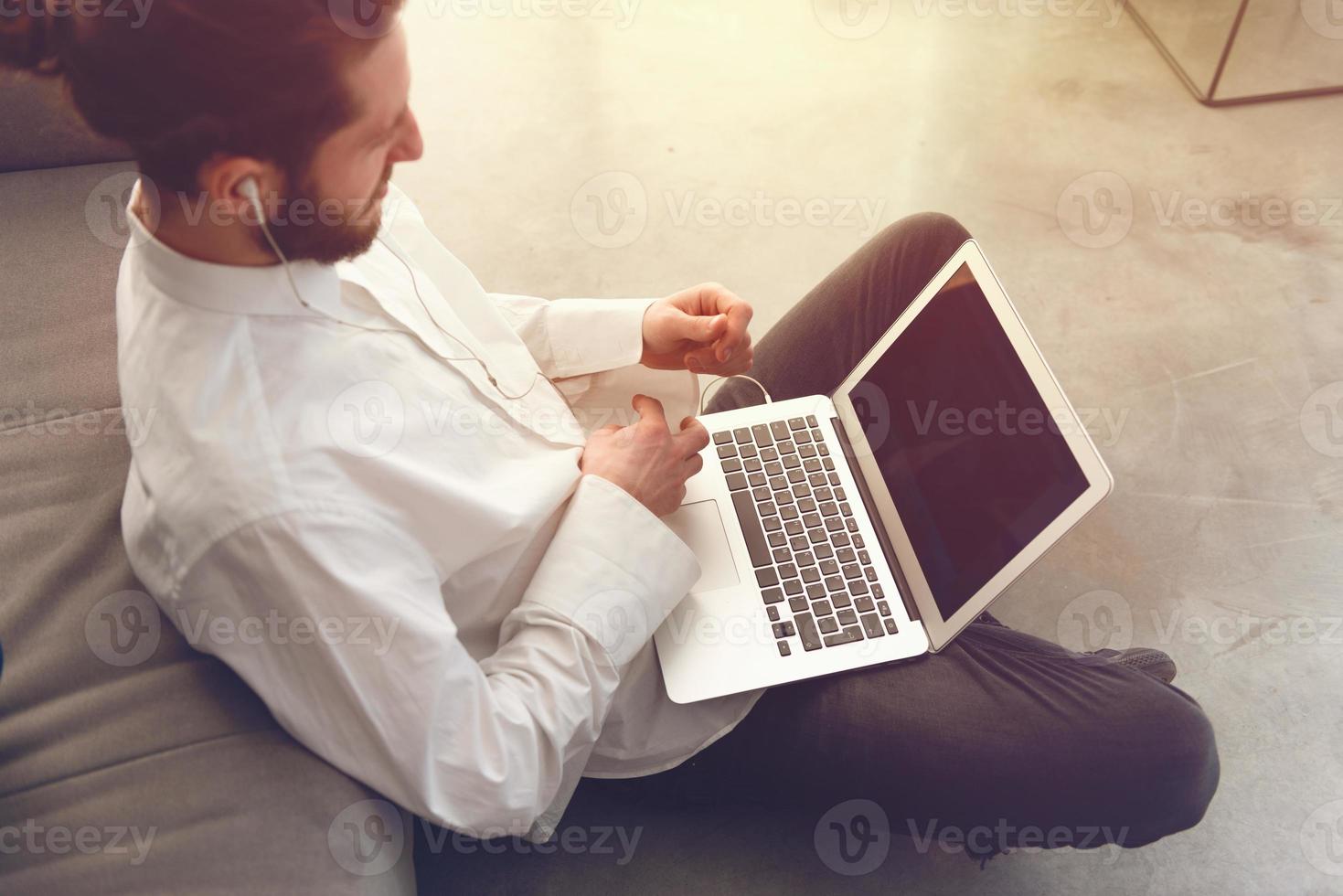 Young businessman sitting on the floor while working from home with a laptop photo