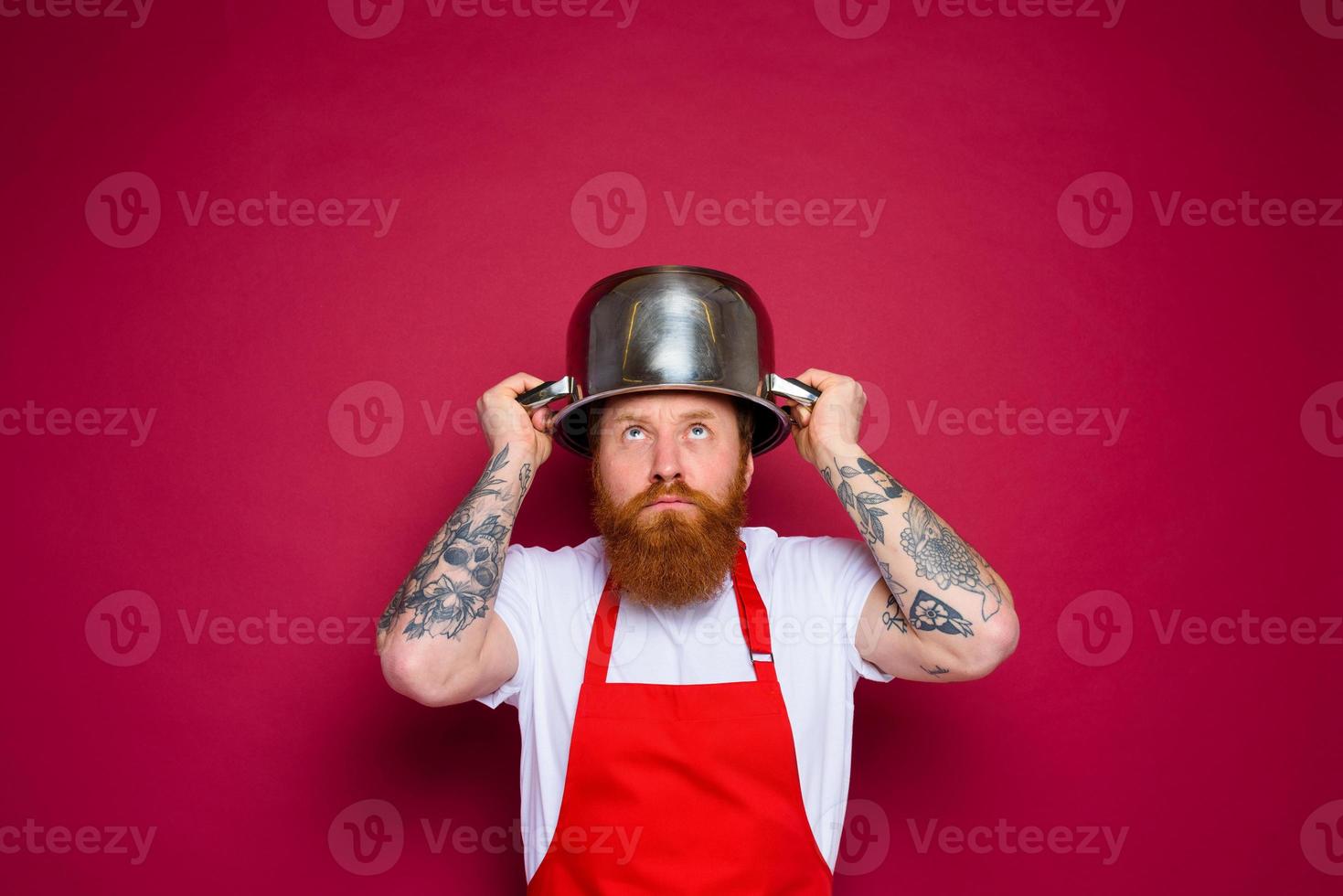 worried chef with beard and red apron plays with pot photo