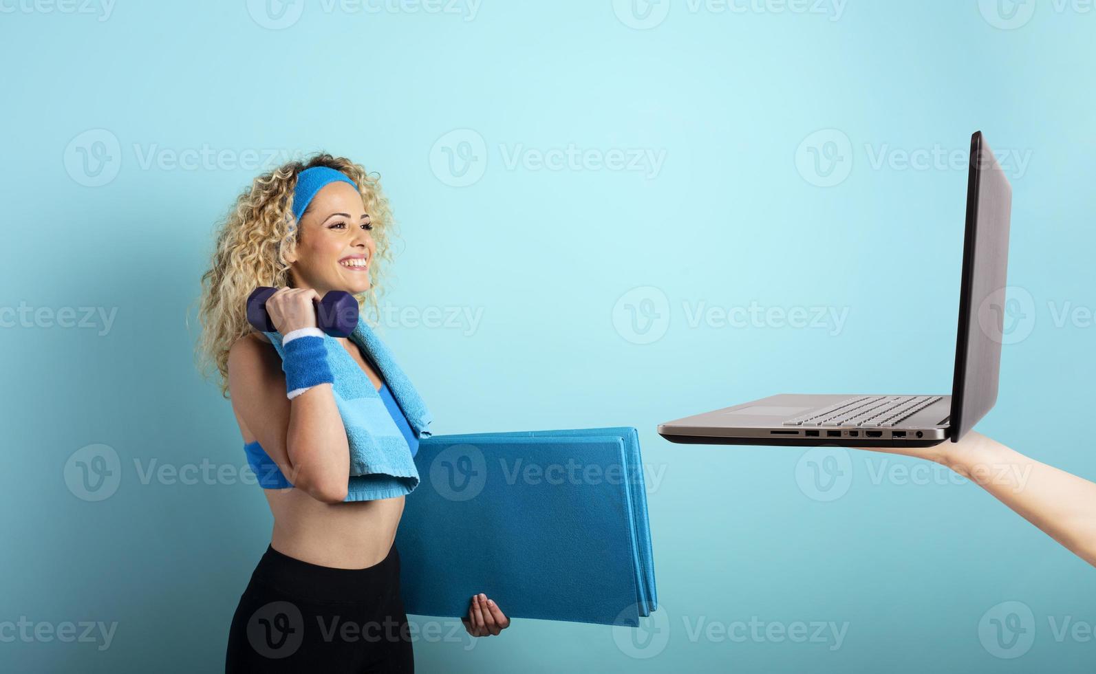 Girl with handlebars ready to start the gym online with a computer. cyan background photo