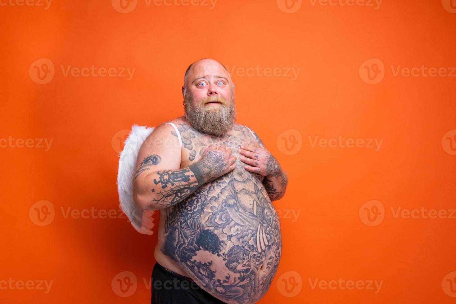 Fat amazed man with beard ,tattoos and wings acts like an angel photo