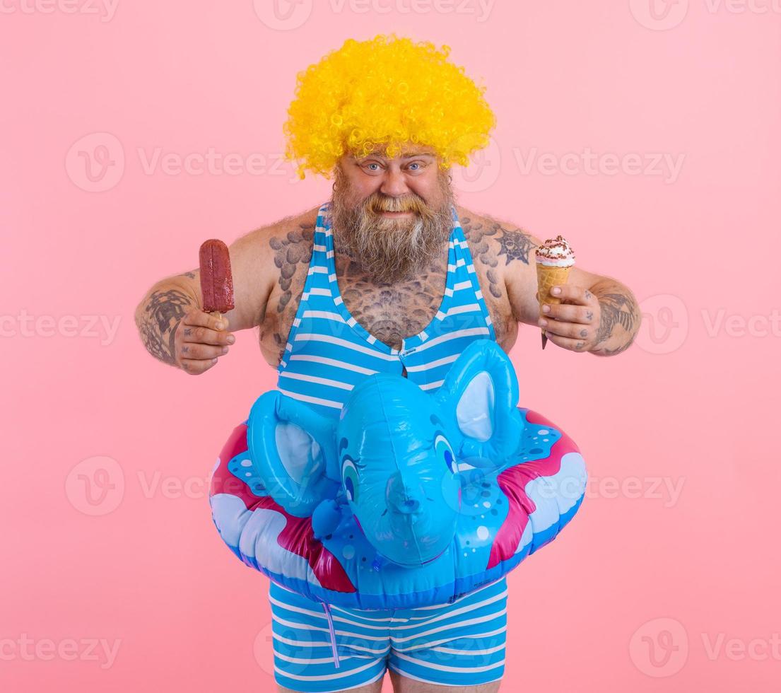 Fat man with beard and wig eats a popsicle and an icecream photo