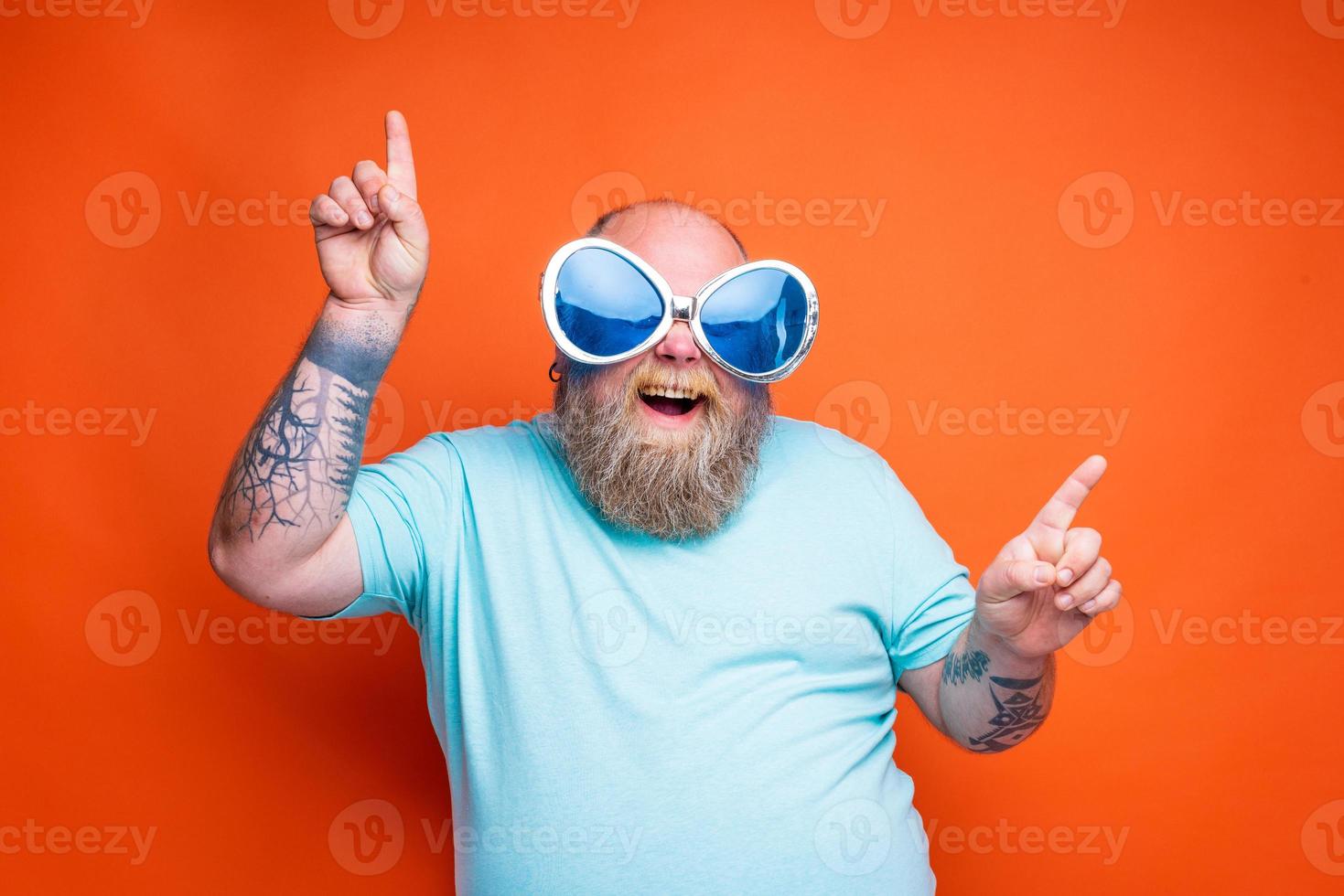 Fat happy man with beard, tattoos and sunglasses dances music photo