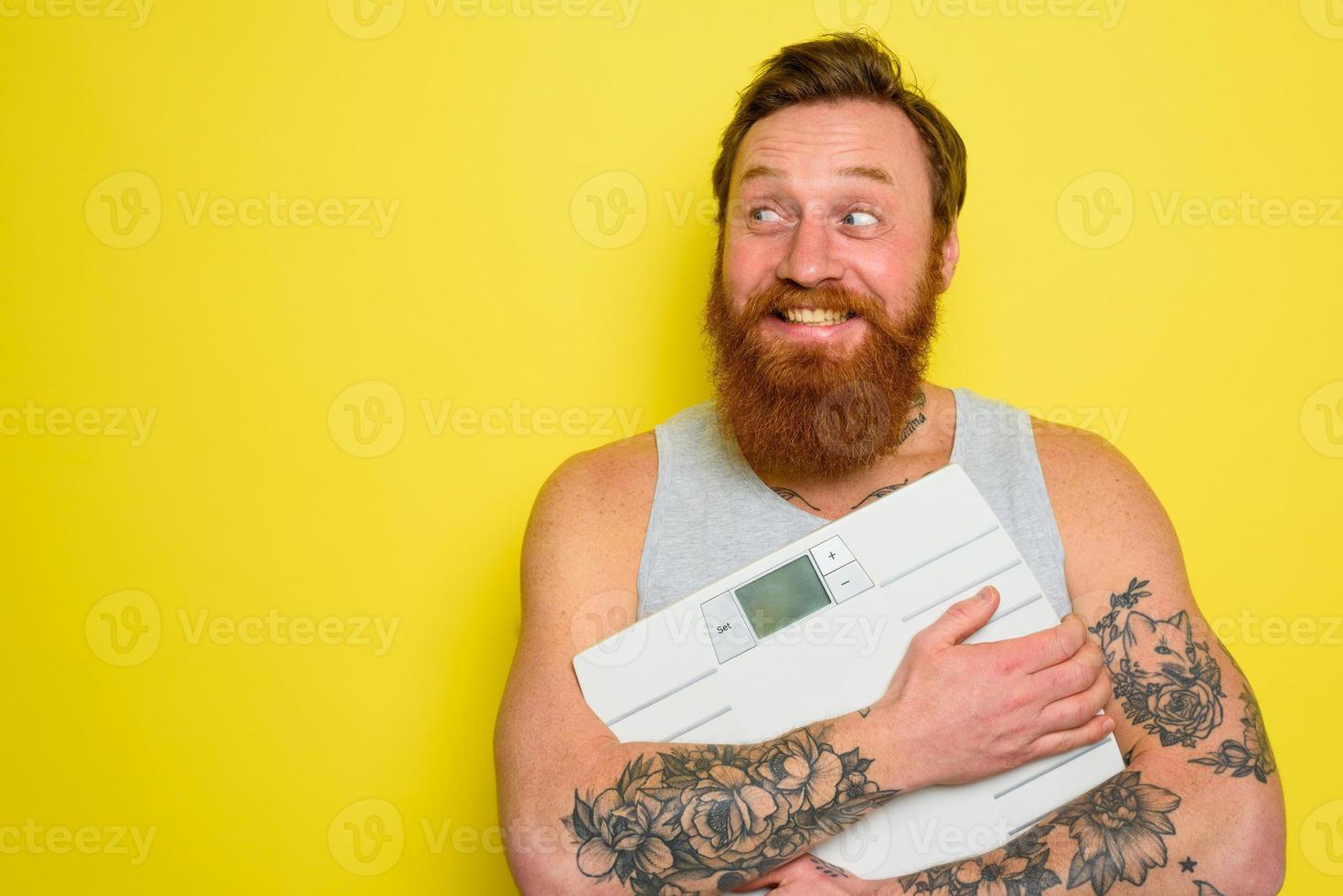 Happy man with beard and tattoos holds an electronic balance photo