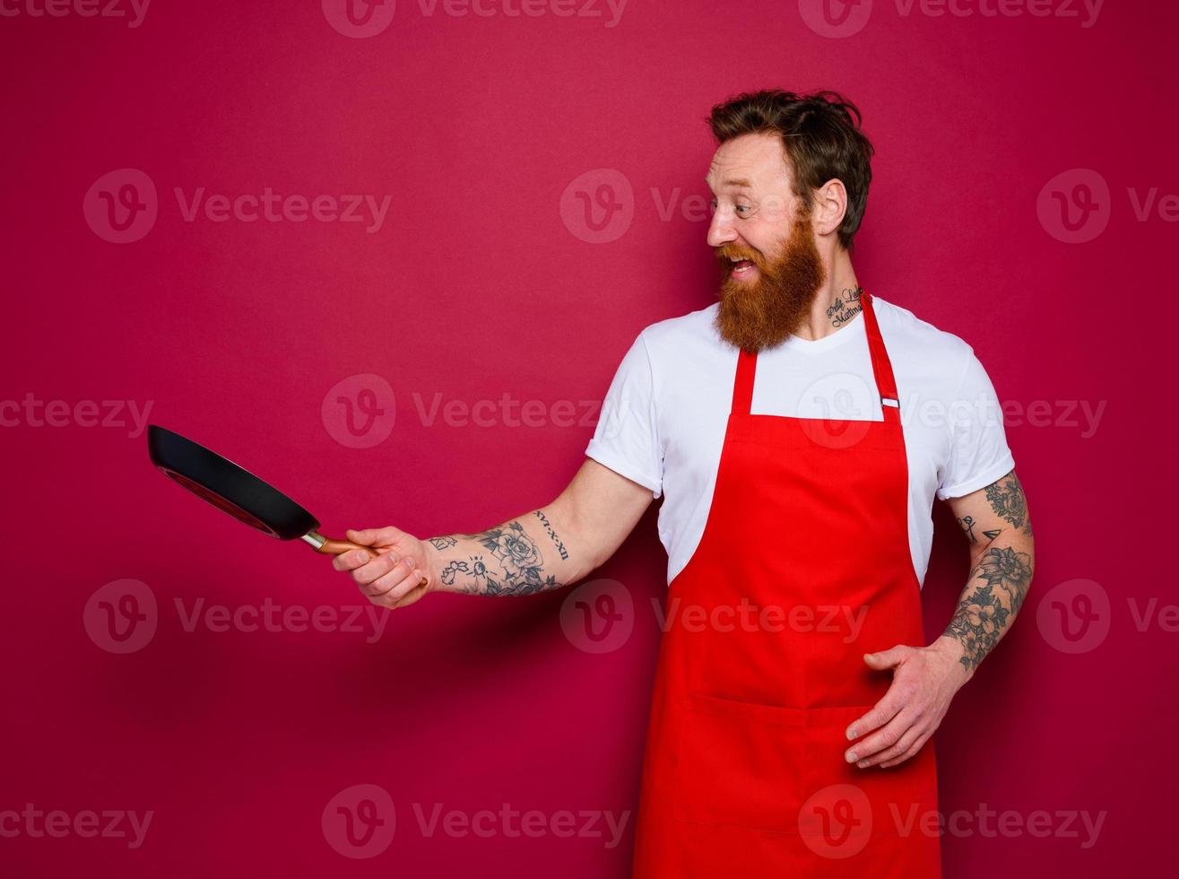 Happy chef with beard and red apron cooks with pan photo