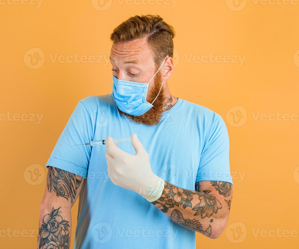Afraid man with beard, tattoo and mask for covid-19 is ready for the virus vaccine photo