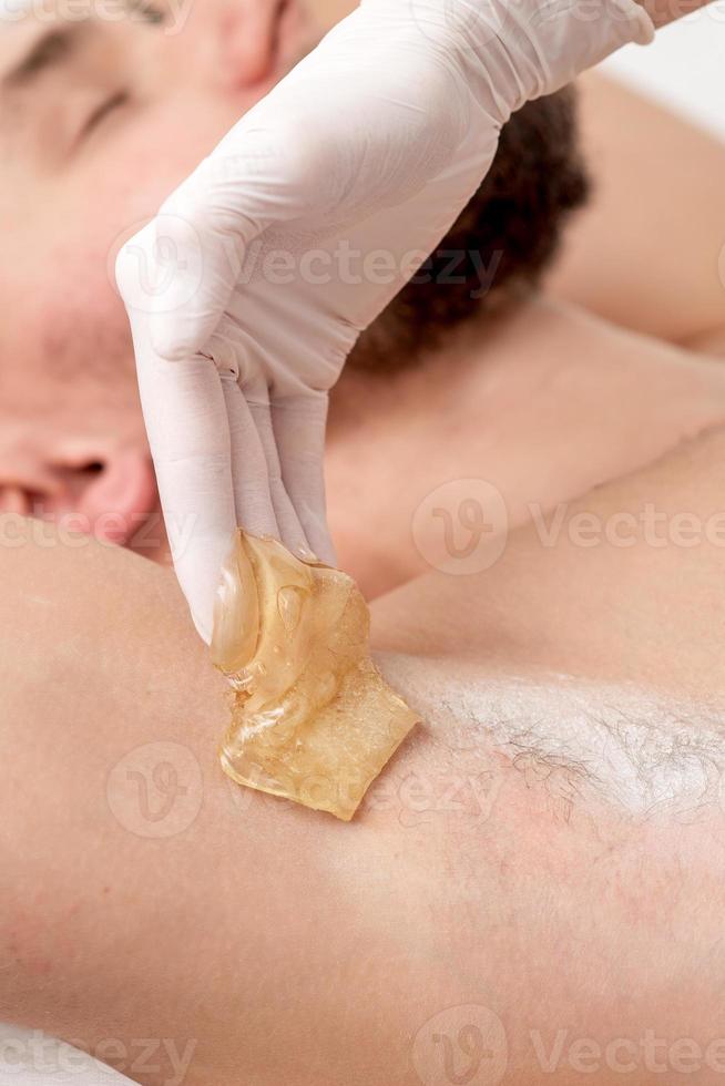 Cosmetologist applying wax paste on male armpit photo