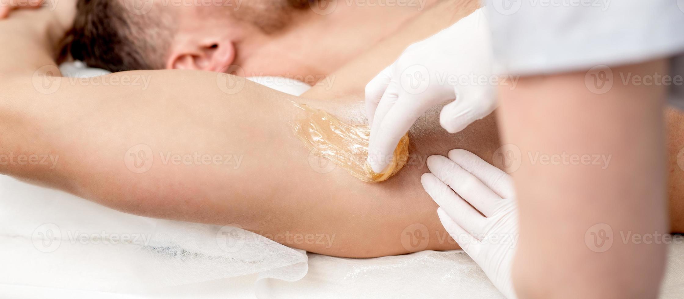 Cosmetologist applying wax paste on male armpit photo