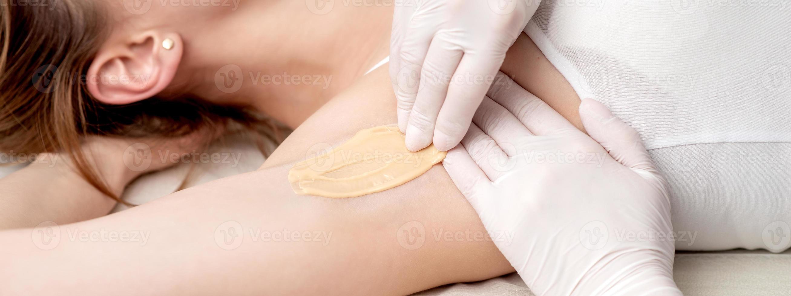 Cosmetologist applying wax paste on armpit photo