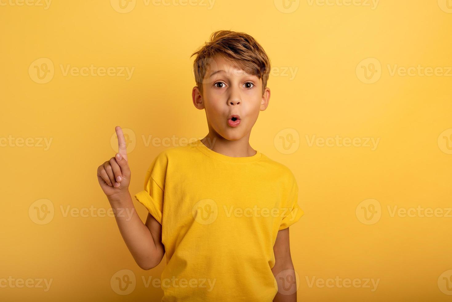 Child indicates above. Amazed and shocked expression. Yellow background photo