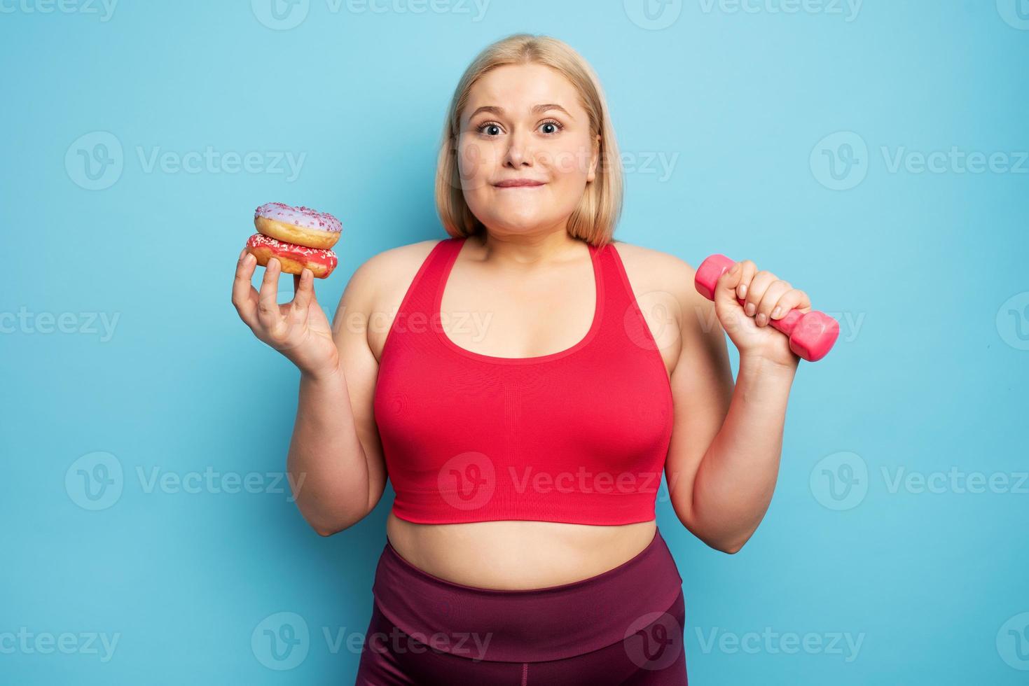 Fat girl thinks to eat donuts instead of does gym. Concept of indecision and doubt photo