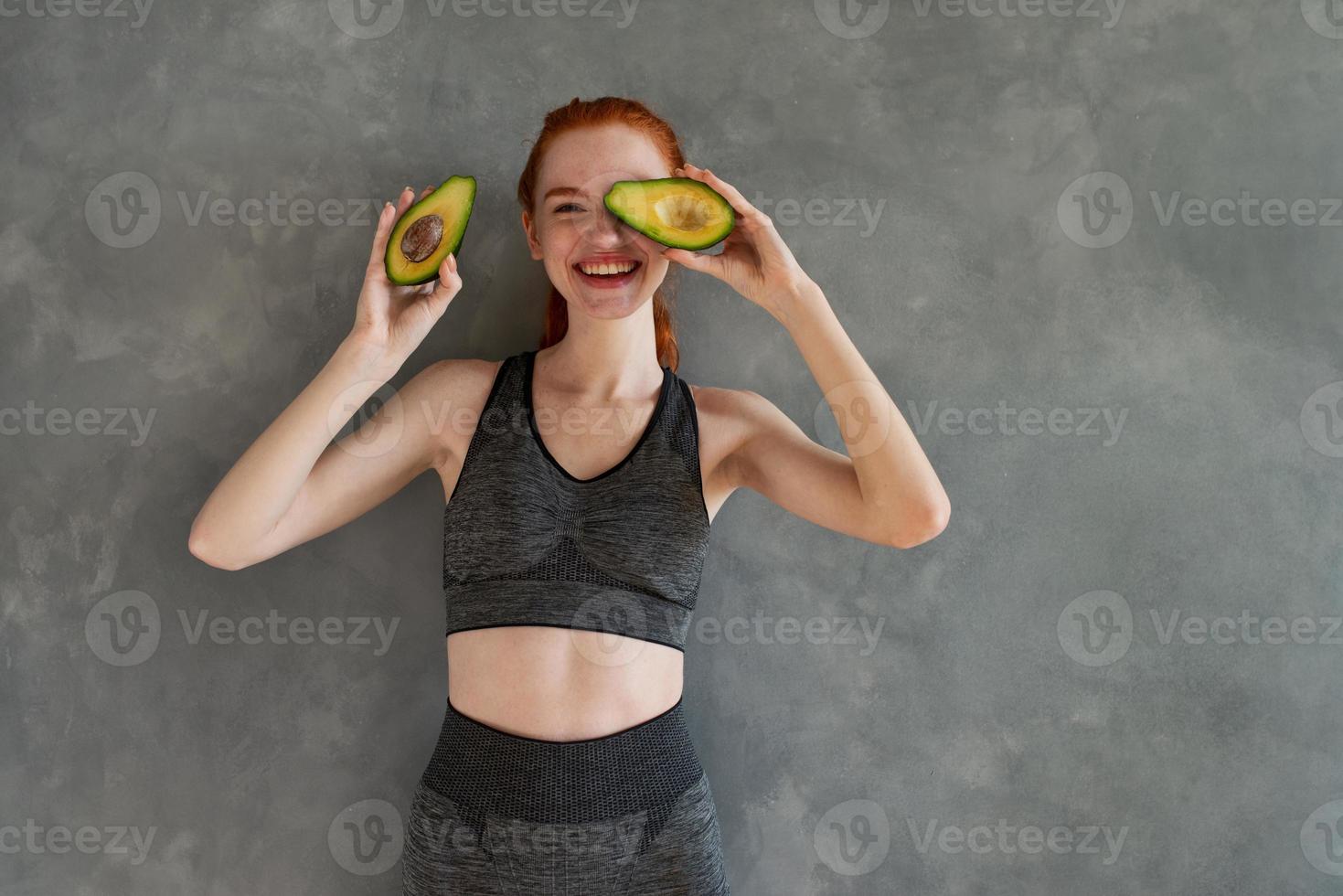 Athletic girl with gym clothes eats avocado at home photo