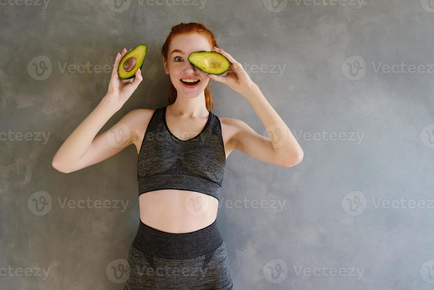 Athletic girl with gym clothes eats avocado at home photo