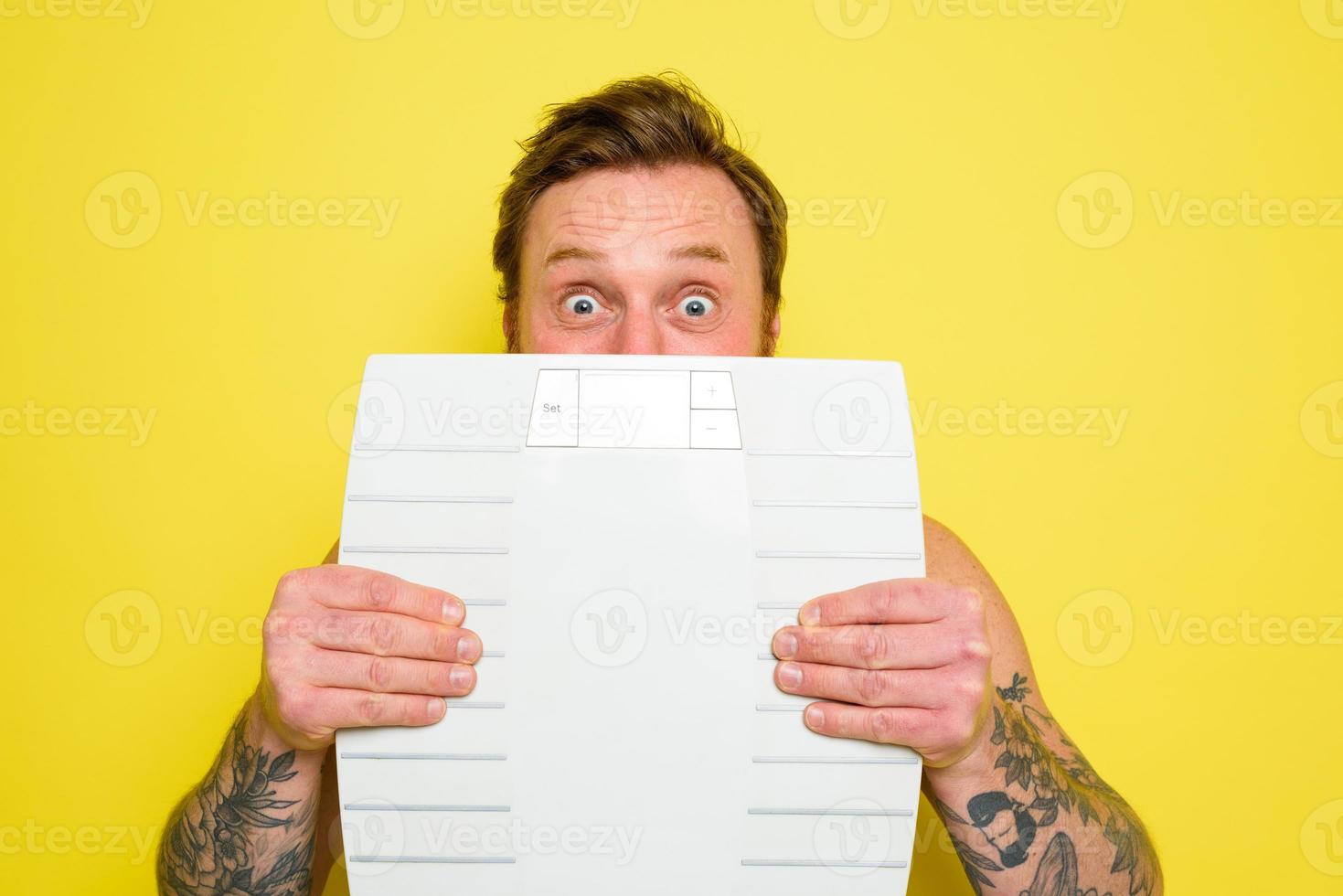 Amazed man with beard and tattoos is hidden behind the scales photo