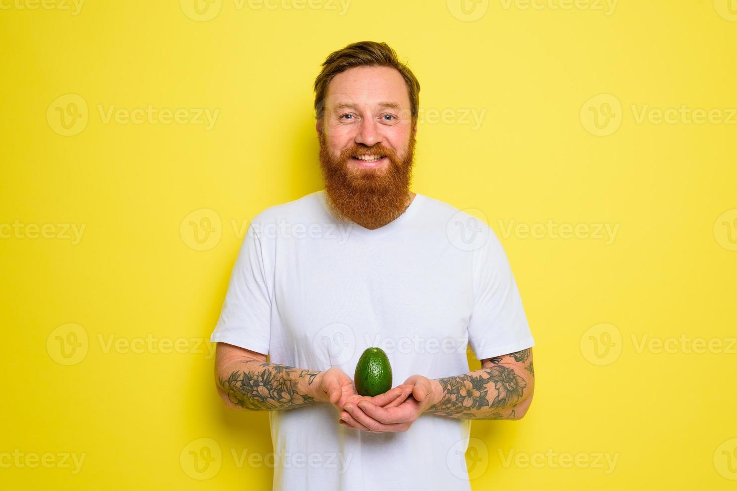 Happy man with beard and tattoos holds an avocado photo