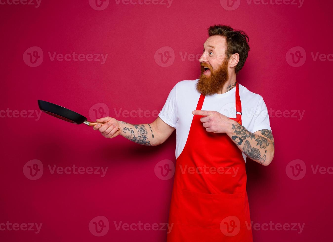 amazed chef with beard and red apron cooks with pan photo