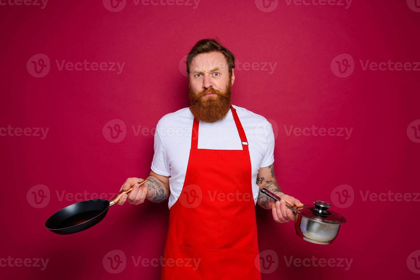 doubter chef with beard and red apron cooks with pan and pot photo