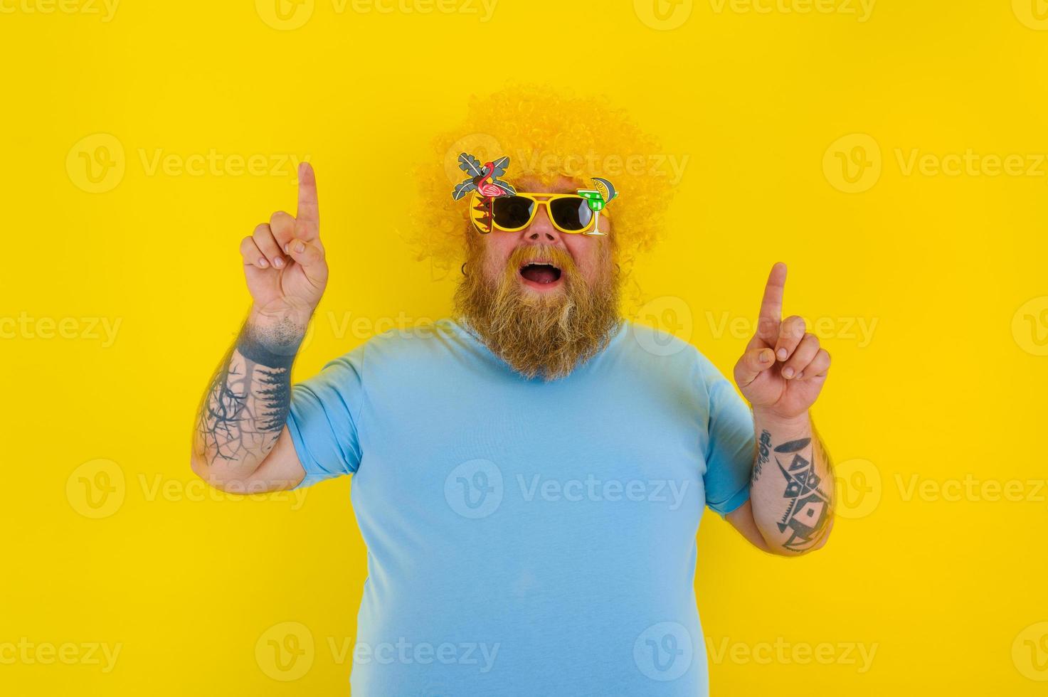 Fat man with wig in head and sunglasses indicates with hands something photo