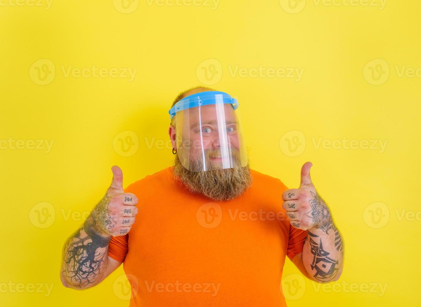 Happy man with beard and tattoos wears a protective face shield against covid-19 photo