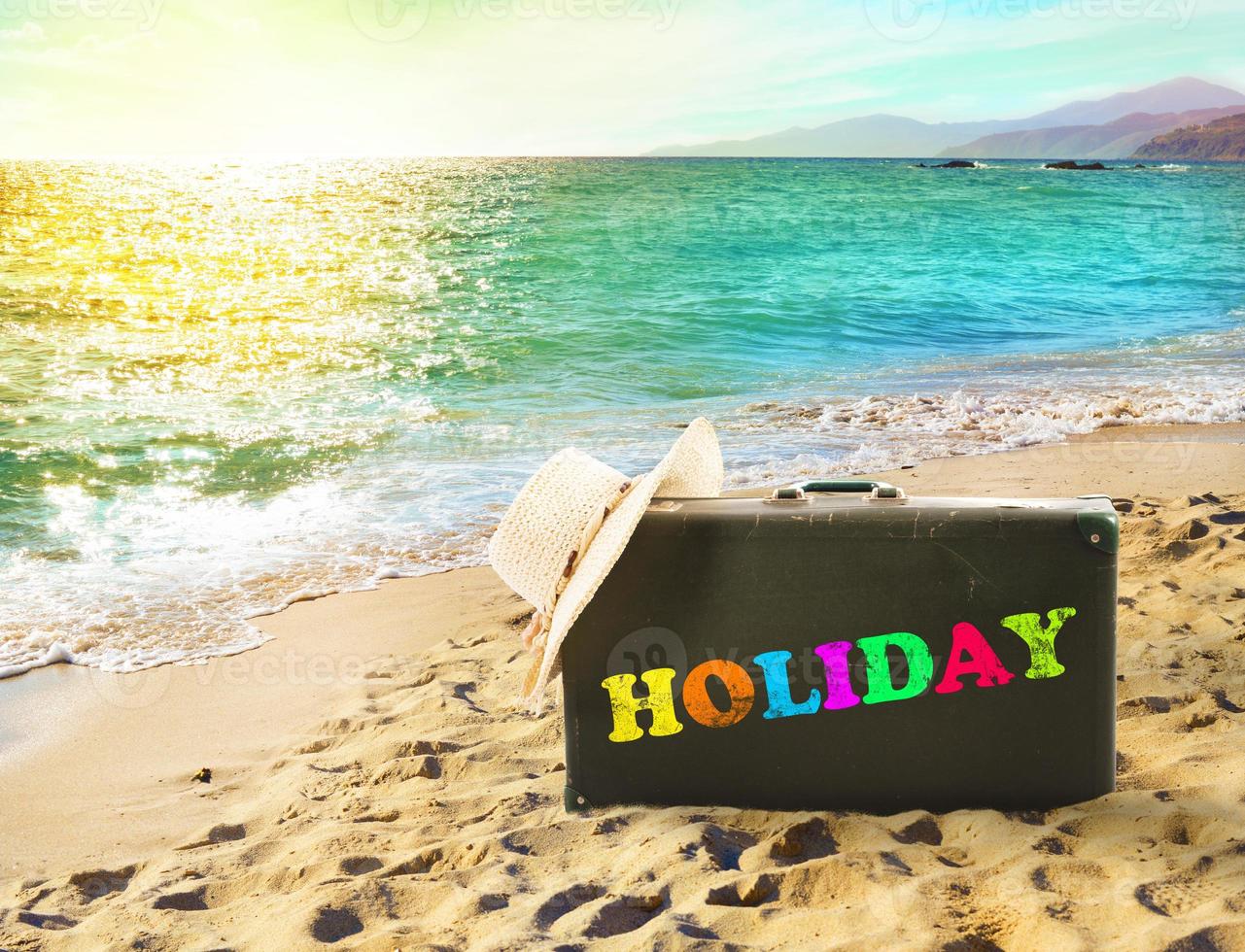 Suitcase in a tropical beach with holiday writing photo