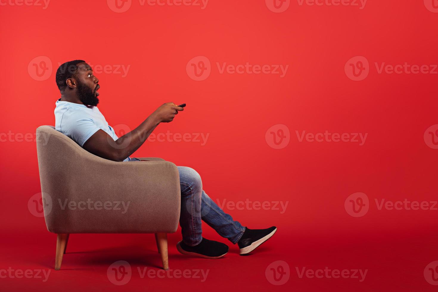 Televiewer on home chair changes channel with remote control on red background photo