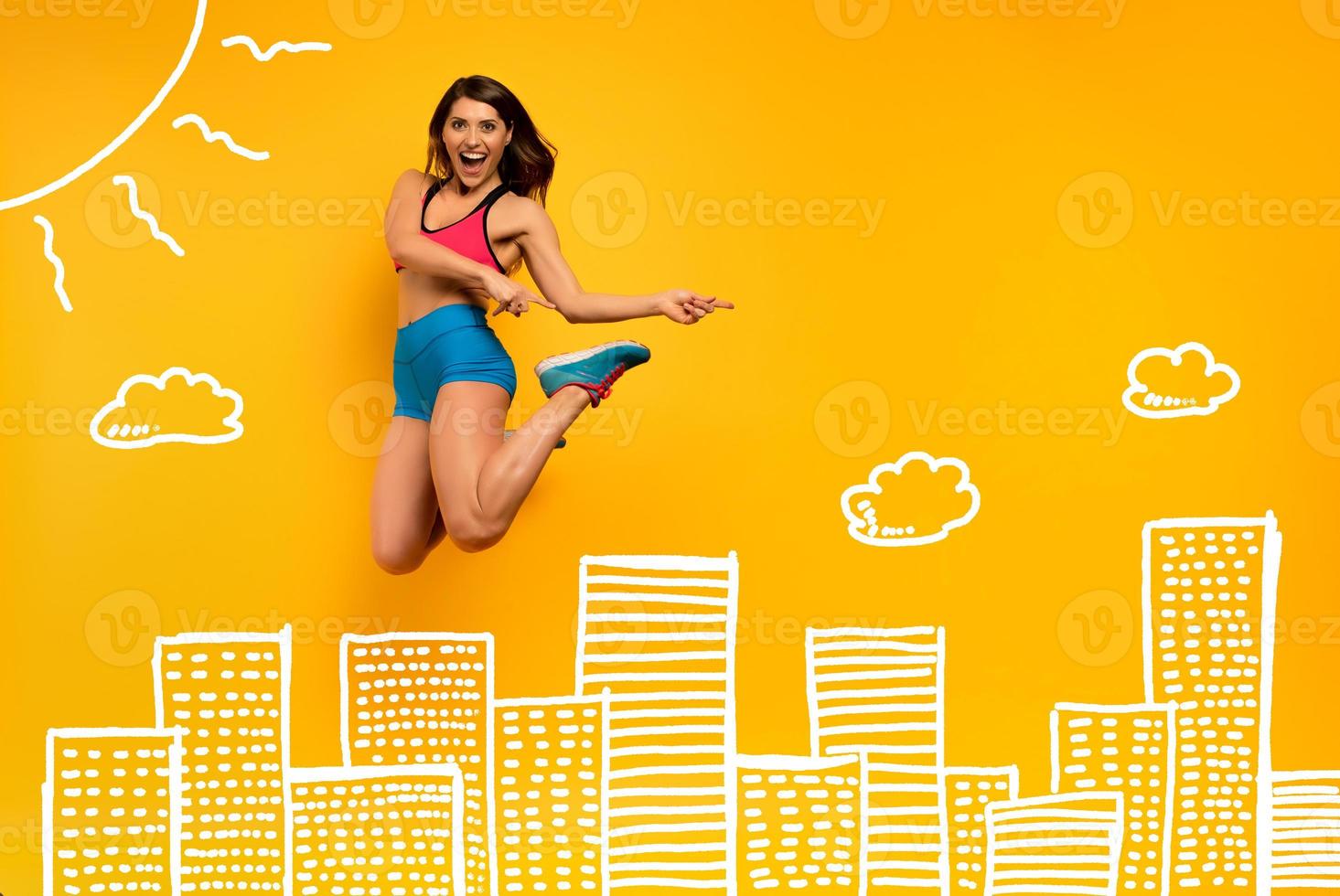 Sport woman jumps on a yellow background with Skyscrapers drawing. Happy and joyful expression. photo