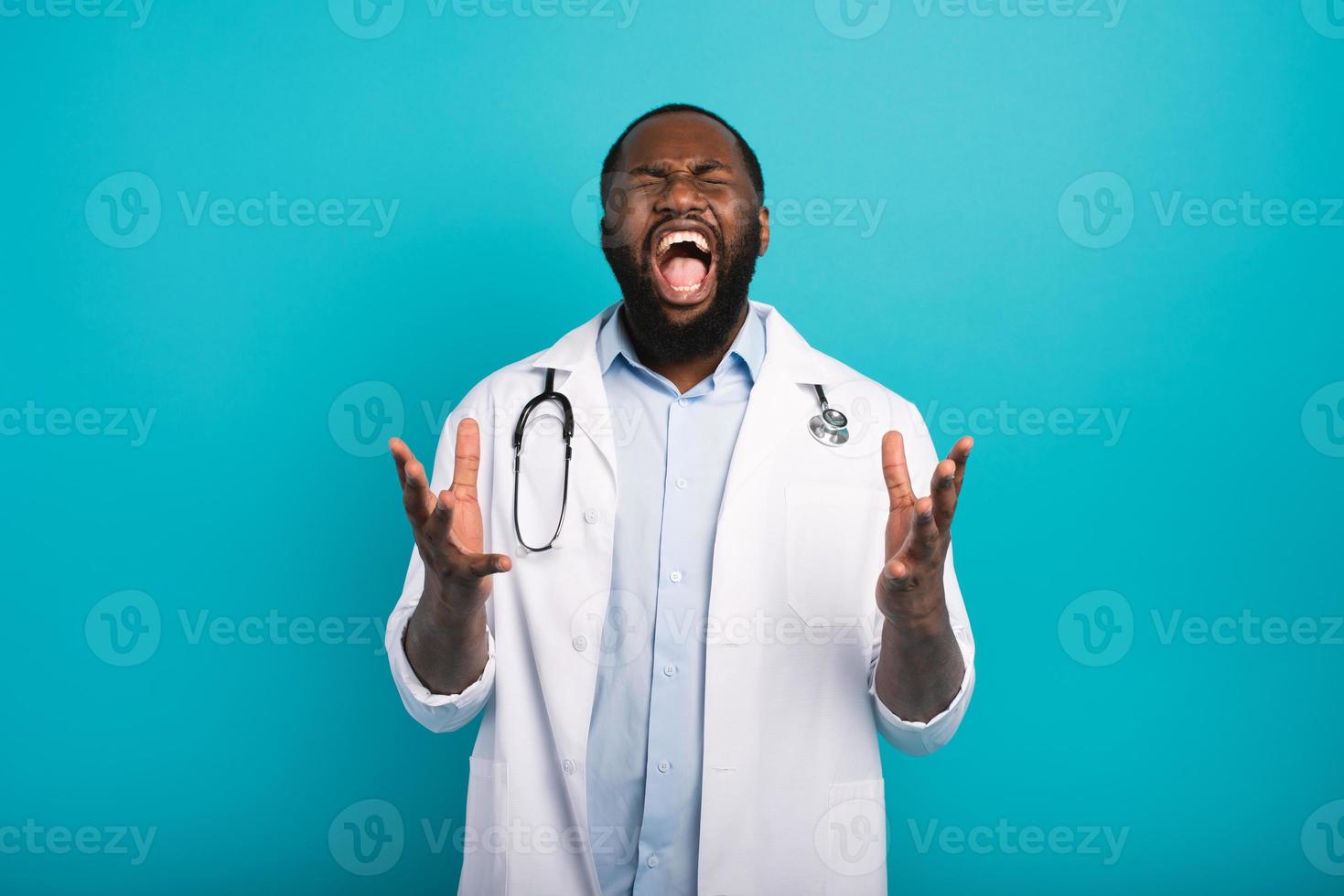 Exhausted doctor with lab coat and stethoscope screams on cyan background photo