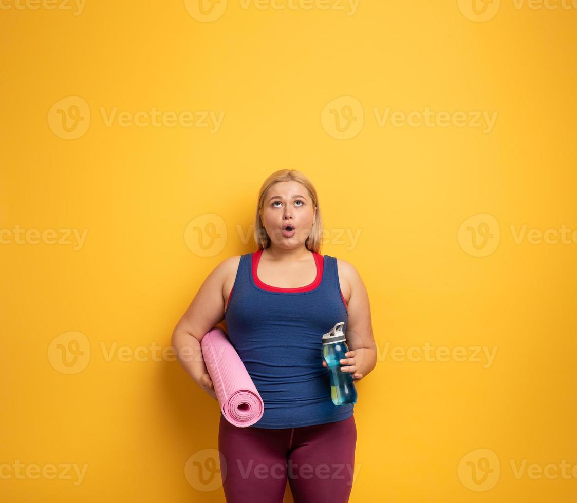 Fat girl does gym at home. surprised expression. Yellow background photo