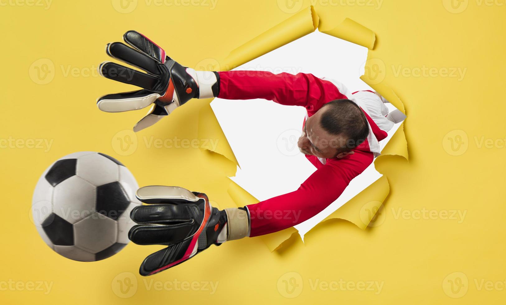 Goalkeeper exits from a hole and tries to tatches the ball. yellow background photo