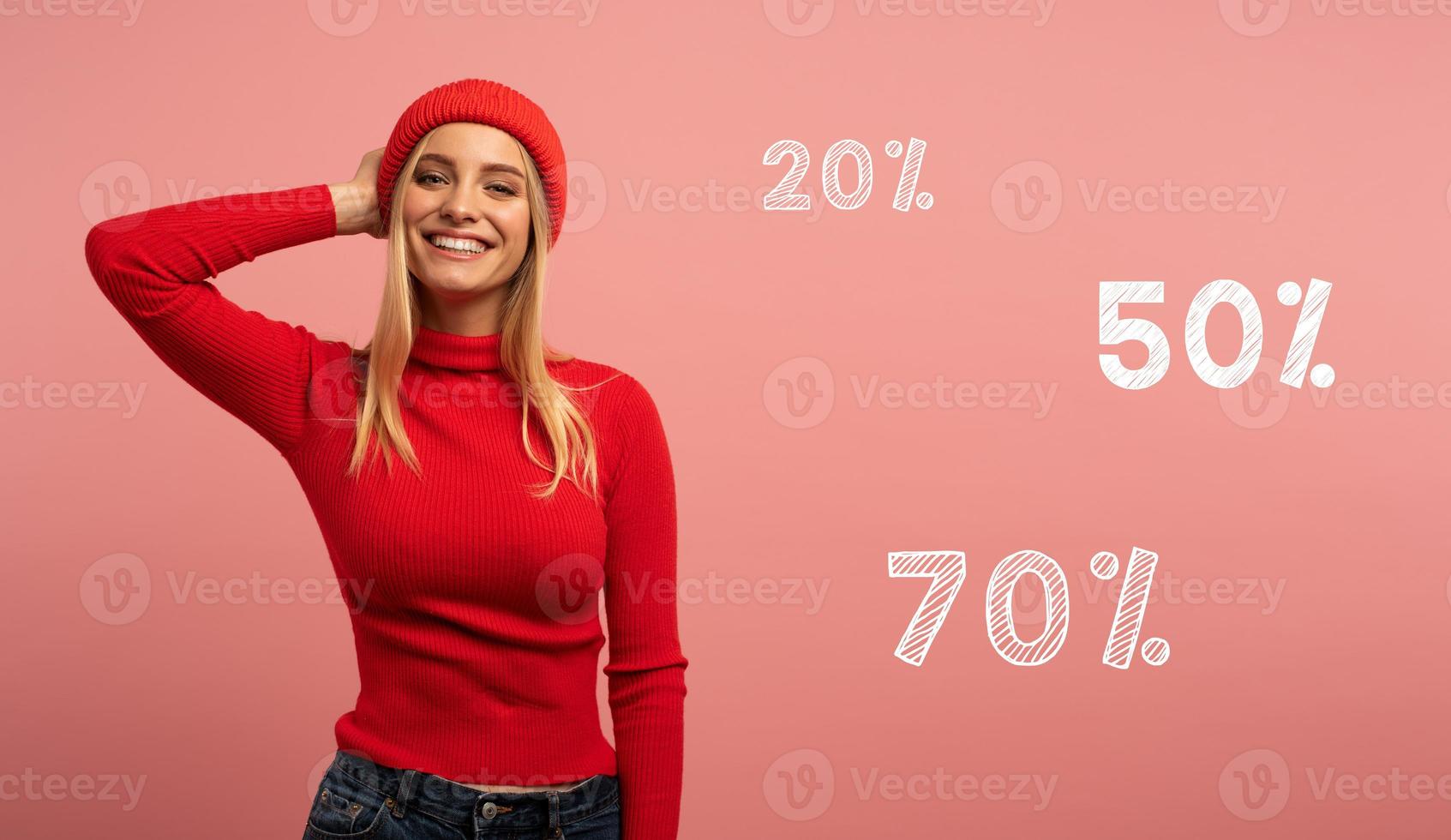 Blonde girl smiles with red hat and cardigan. Pink background for blank space for your discount text photo