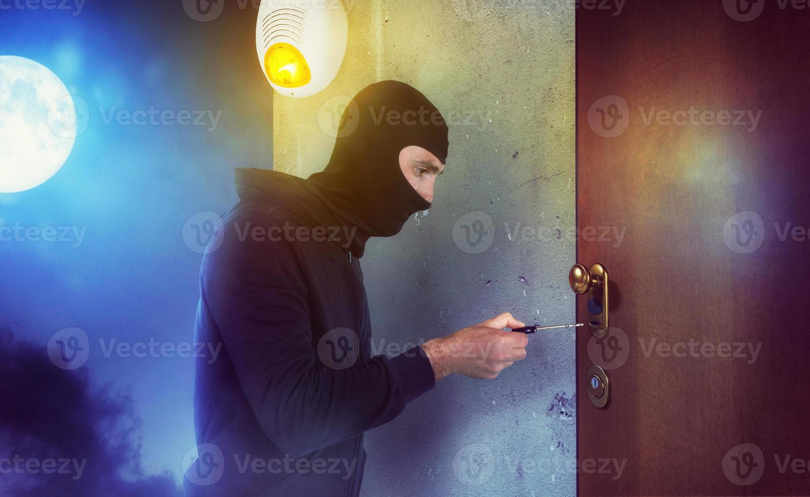 Thief with balaclava tries to open the door of apartment with a key photo