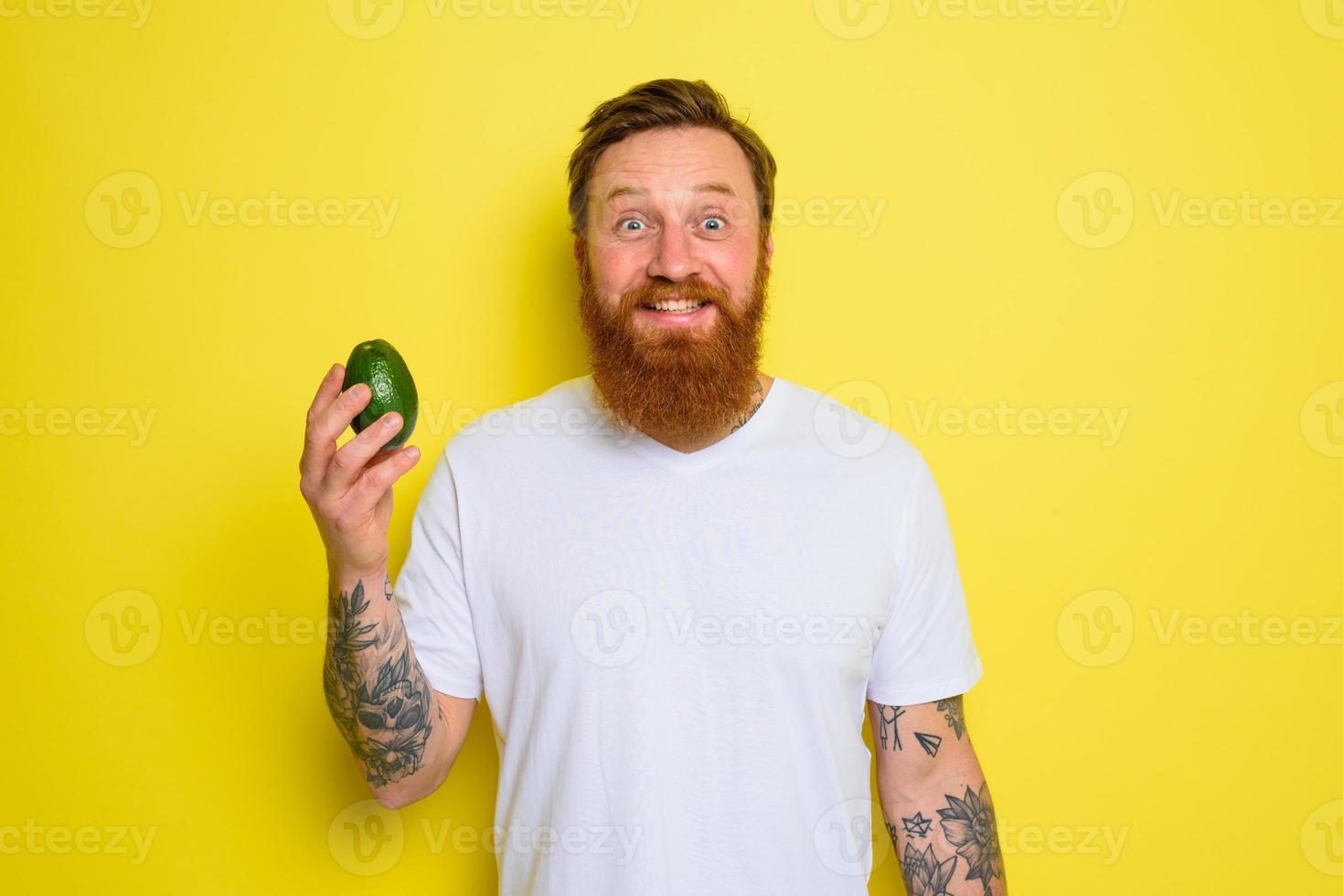 Happy man with beard and tattoos holds an avocado photo