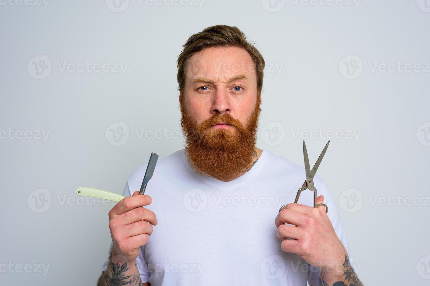 Worried man with scissors and blade is ready to cut the beard photo